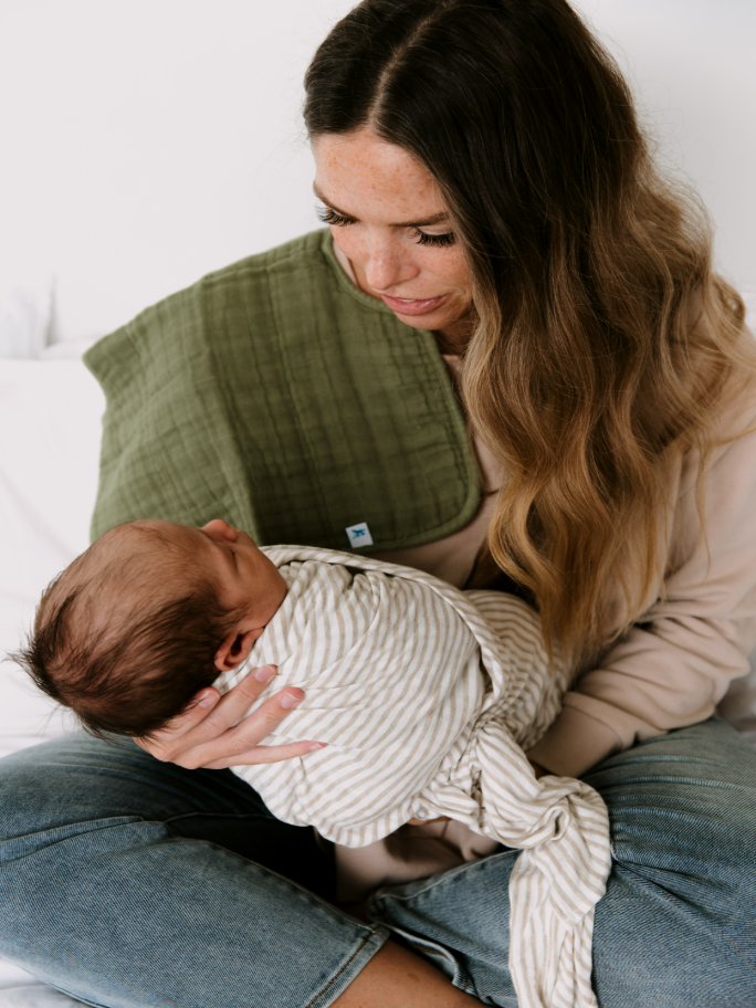 A mother holds a newborn baby in a grey stripe swaddle and green burp cloth over her shoulder