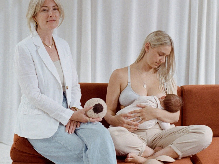 A mother breastfeeding her baby on an orange couch and another woman sitting next to her