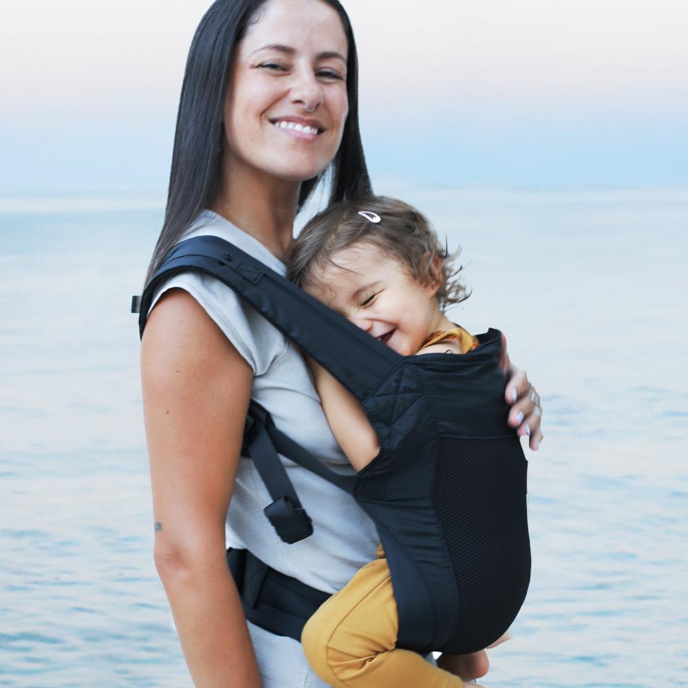Mum at the beach wearing baby in a carrier on her front