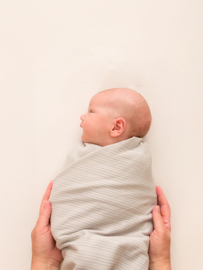 Baby swaddled in pebble ribbed blanket on plain background