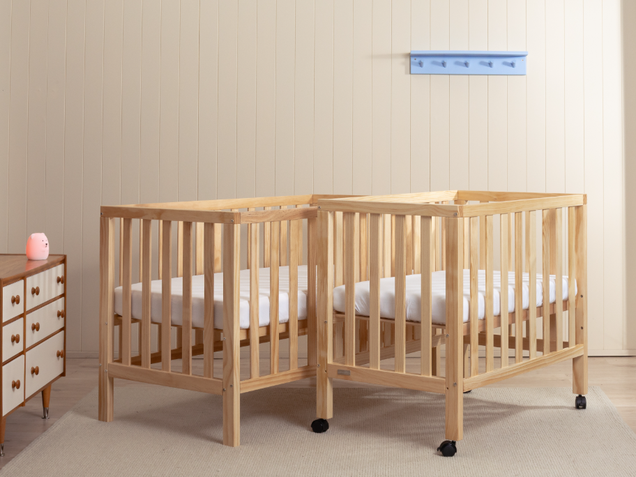 Two beechwood cots of different sizes side by side in a nursery setting