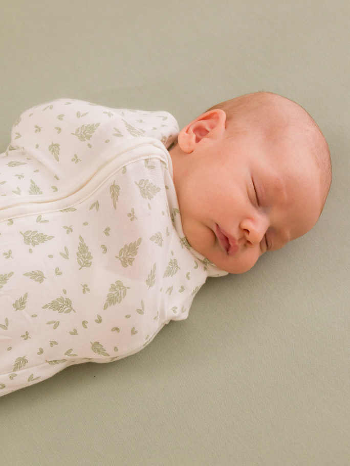Newborn in a fitted cotton zip swaddle with small leaf patterns