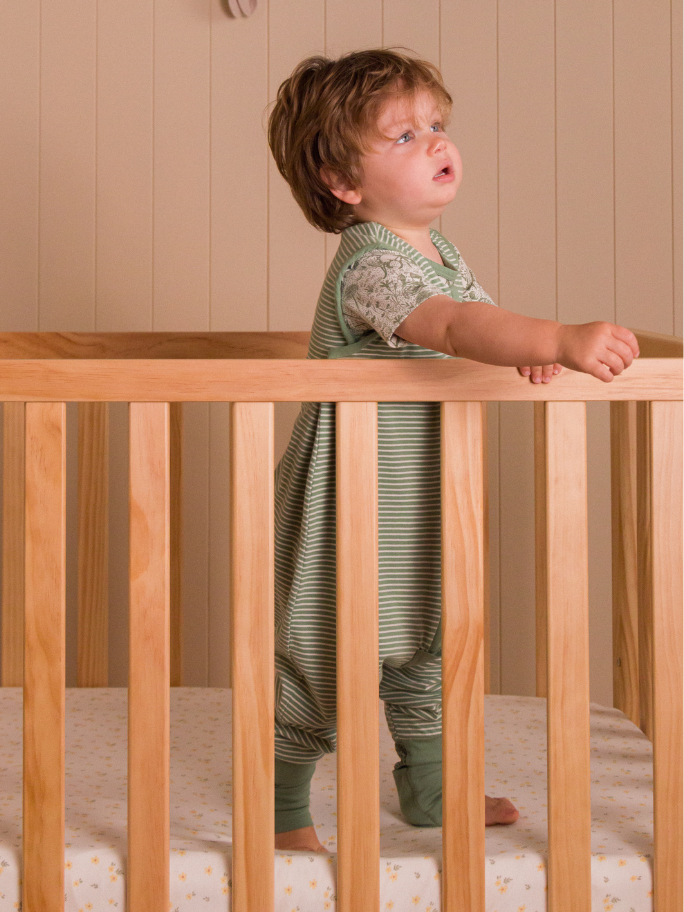 Toddler standing in cot wearing green sleeping suit