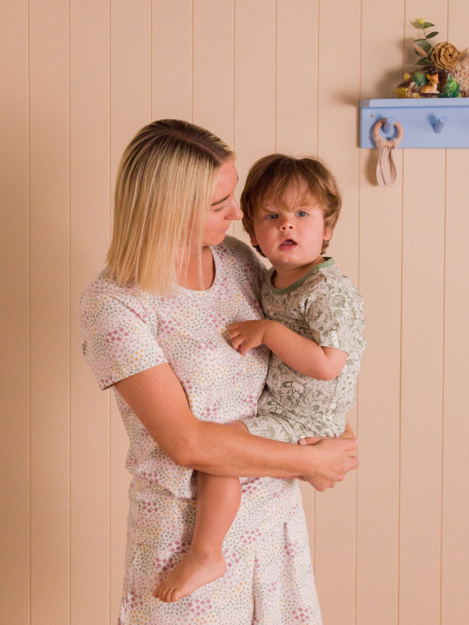 Mum in floral pyjamas holding onto toddler in green patterned pyjamas