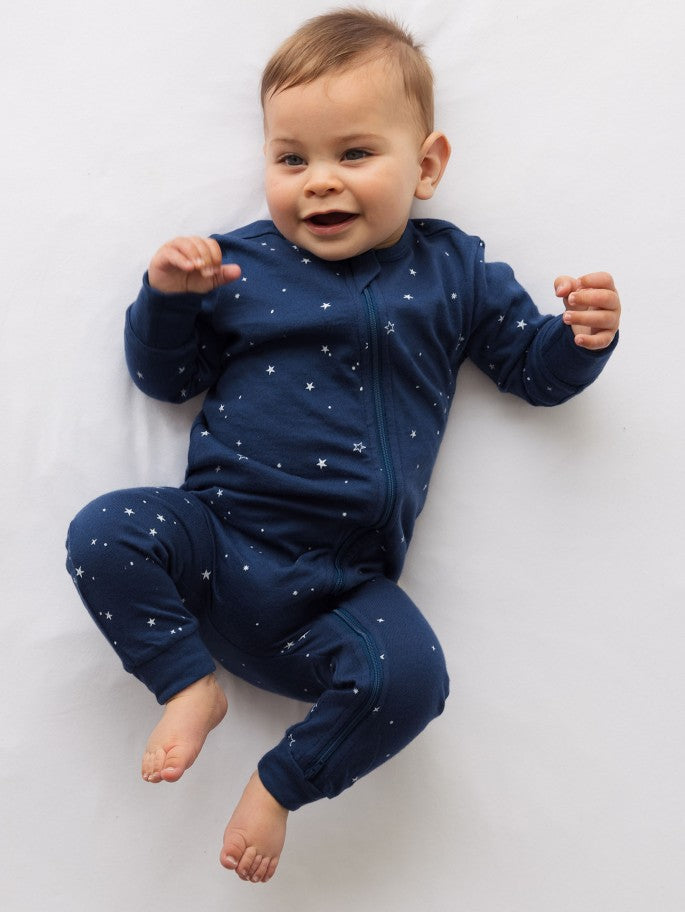 Baby wearing a navy and white star pyjama suit on a plain background