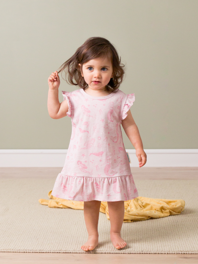 Toddler in pink Woolbabe nightie, holding a strand of her hair in studio setting