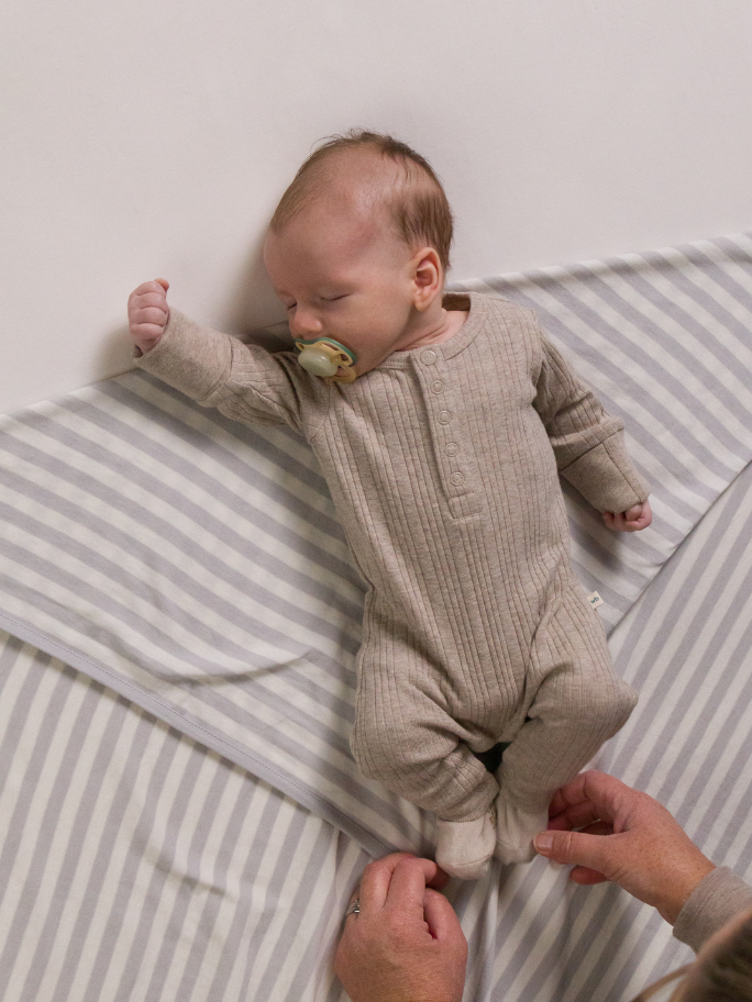 Newborn in beige ribbed pyjama suit and dummy laying on a striped swaddle