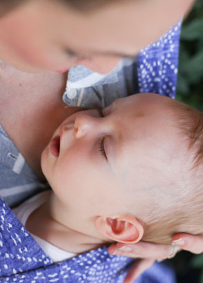 Baby sleeping in wrap while mother watches over him holding his head