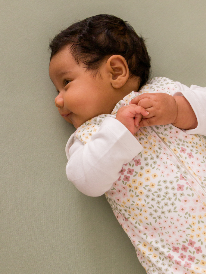 Baby smiling in white floral cotton swaddle bag