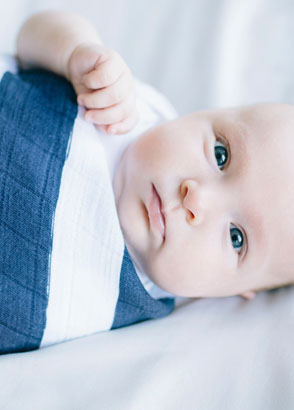 Blue eyed baby wrapped in navy and white muslin swaddle