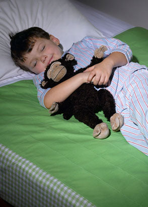 Child sleeping cuddling soft toy in bed fitted with green brolly sheet