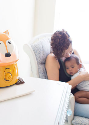 Mother cuddling baby to sleep while running adorables fox humidifier in nursery