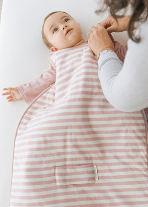 Mother dressing tired baby in dusk Woolbabe duvet sleepbag