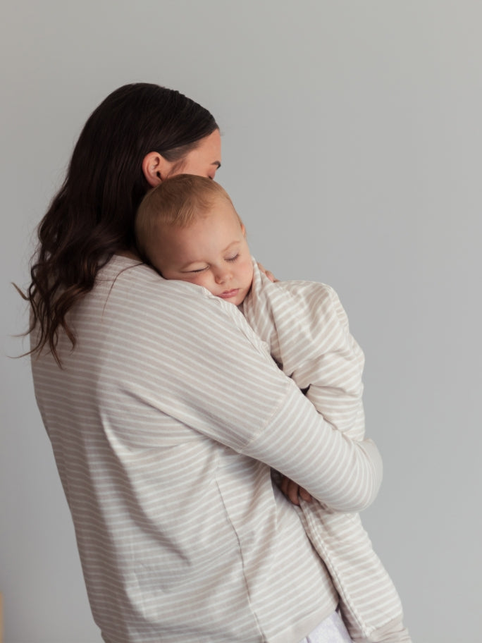 Mum wearing woolbabe pyjamas, holding a sleepy baby over her shoulder