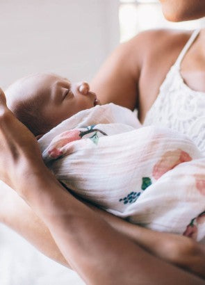 Newborn swaddled in floral muslin blanket being held