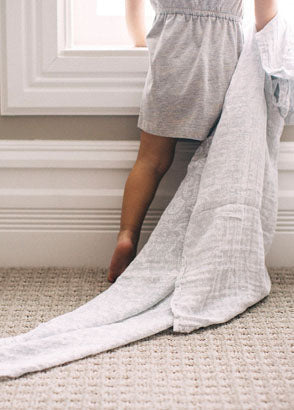 Toddler looking out window with muslin blanket trailing behind