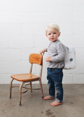Toddler wearing backpack next to a small wooden chair