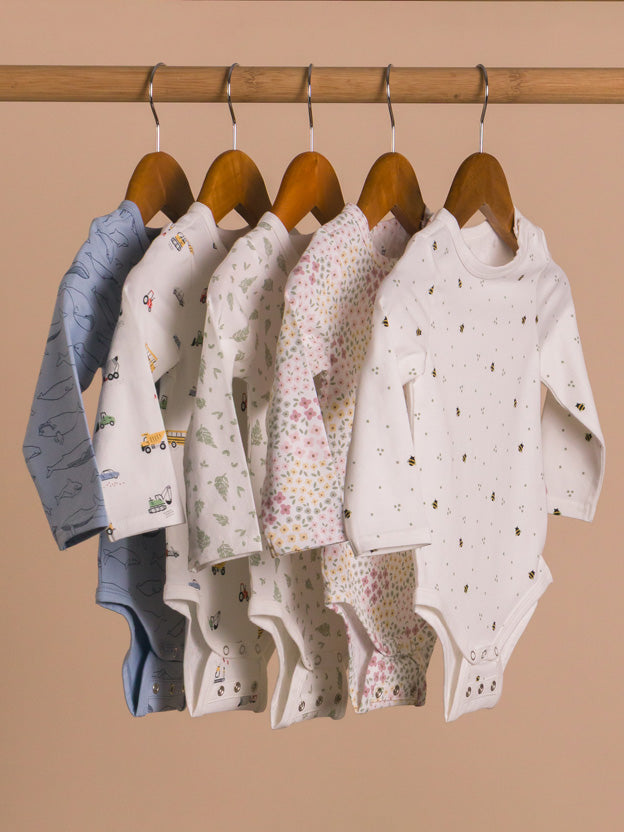 Rack of five organic cotton baby bodysuits hanging on a rail