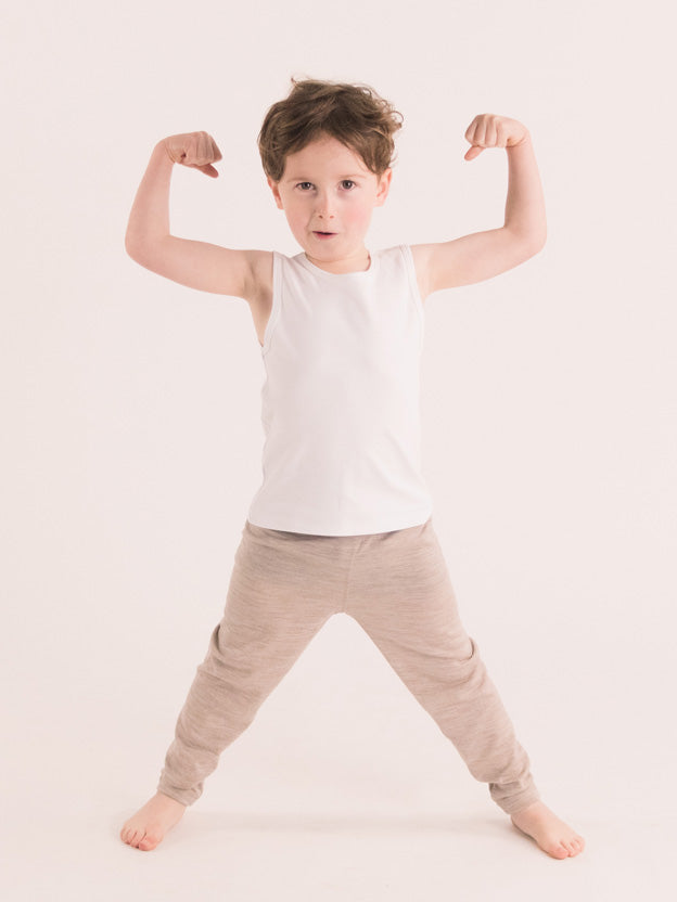 Boy standing with arms up wearing white singlet and oat leggings