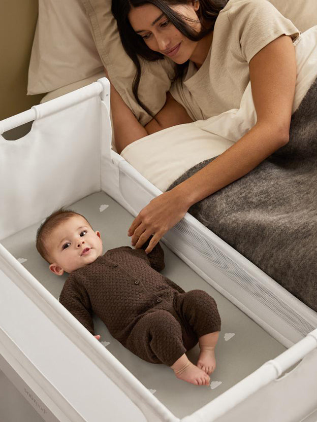 Baby in bassinet next to parents bed with mum looking at baby