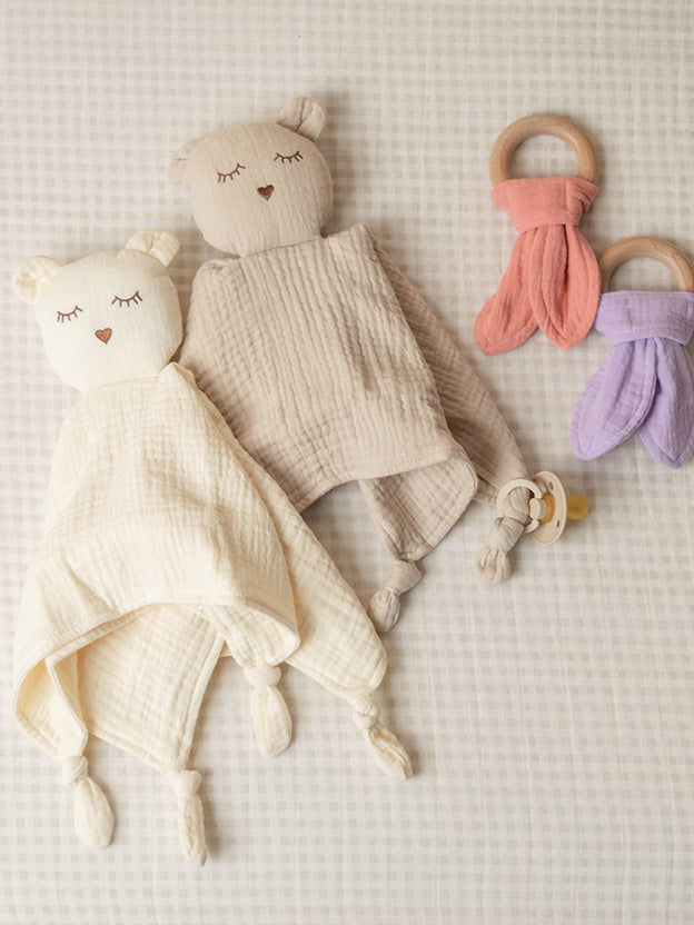 Two muslin sleepy bear comforters and teething rings on a light background