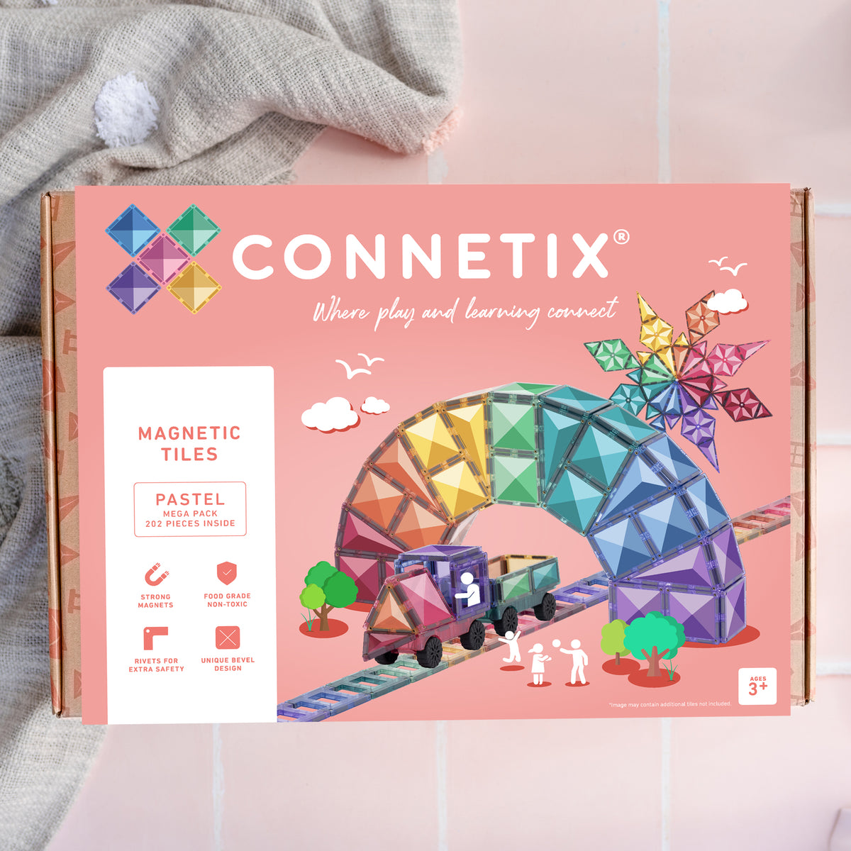 A Connetix Magnetic Tiles 'Pastel' building toy set in its original pink cardboard packaging, styled on a light pink surface with a gray knit blanket in the background.