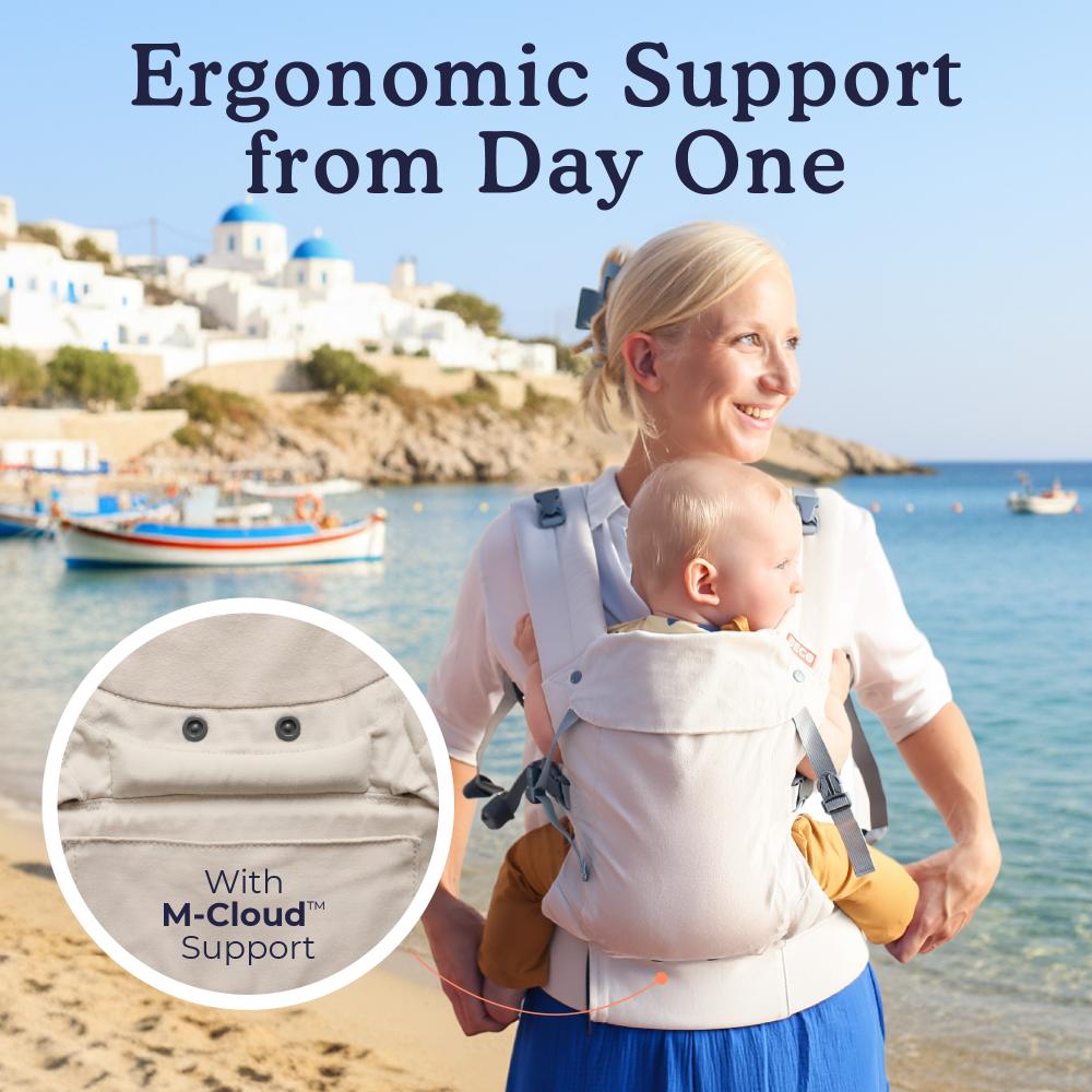 Woman holding a baby in a cream coloured baby carrier with a scenic beach background
