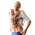 Woman holding a baby in a pink newborn baby carrier against a white background