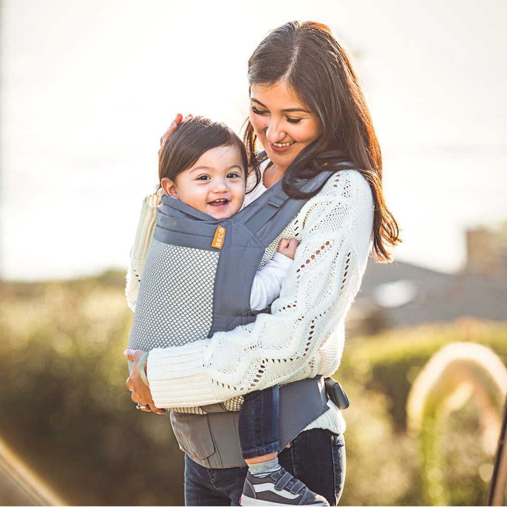 Woman carrying a 2 year old child in a mesh toddler carrier outdoors