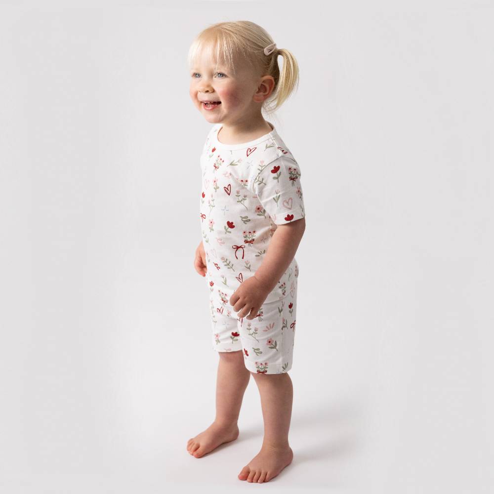 A child wearing short sleeve pjs that have an all over bows, flowers and hearts print. 