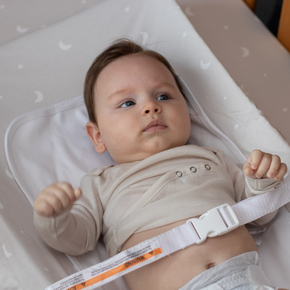 Baby lying on a changing table with a white strap over them