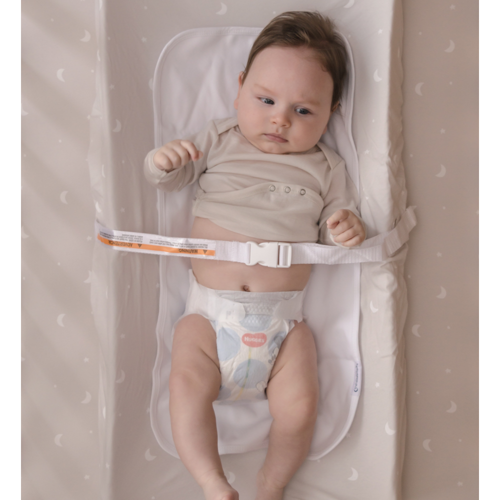 Baby lying on  beige change pad cover sheet with a white border, wearing a diaper.