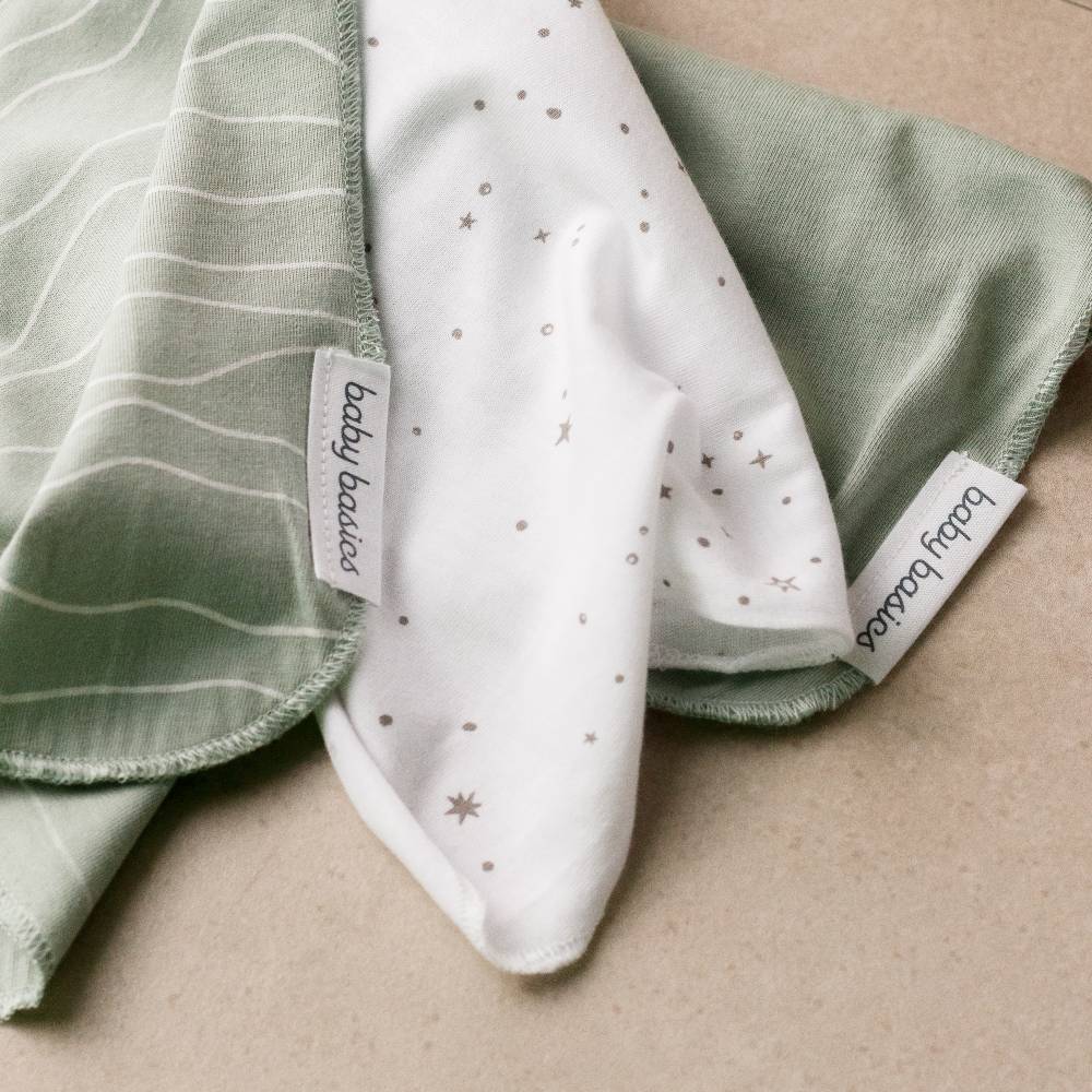 Three wash cloths in green, white, and a patterned white swatch on a beige surface.
