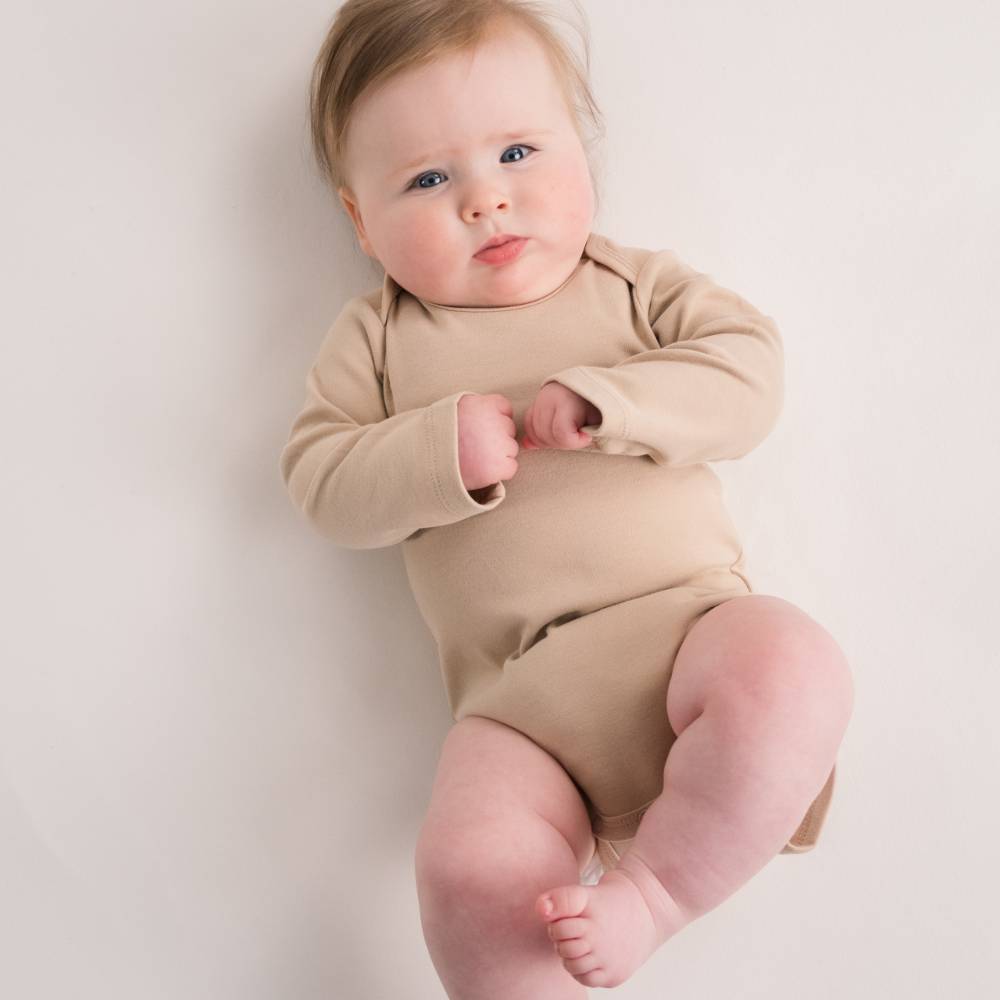 Baby wearing an organic cotton beige long sleeve bodysuit on a plain background