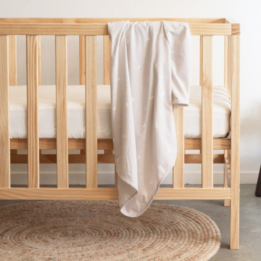 Wooden crib with a beige swaddle blanket draped over it on a neutral background