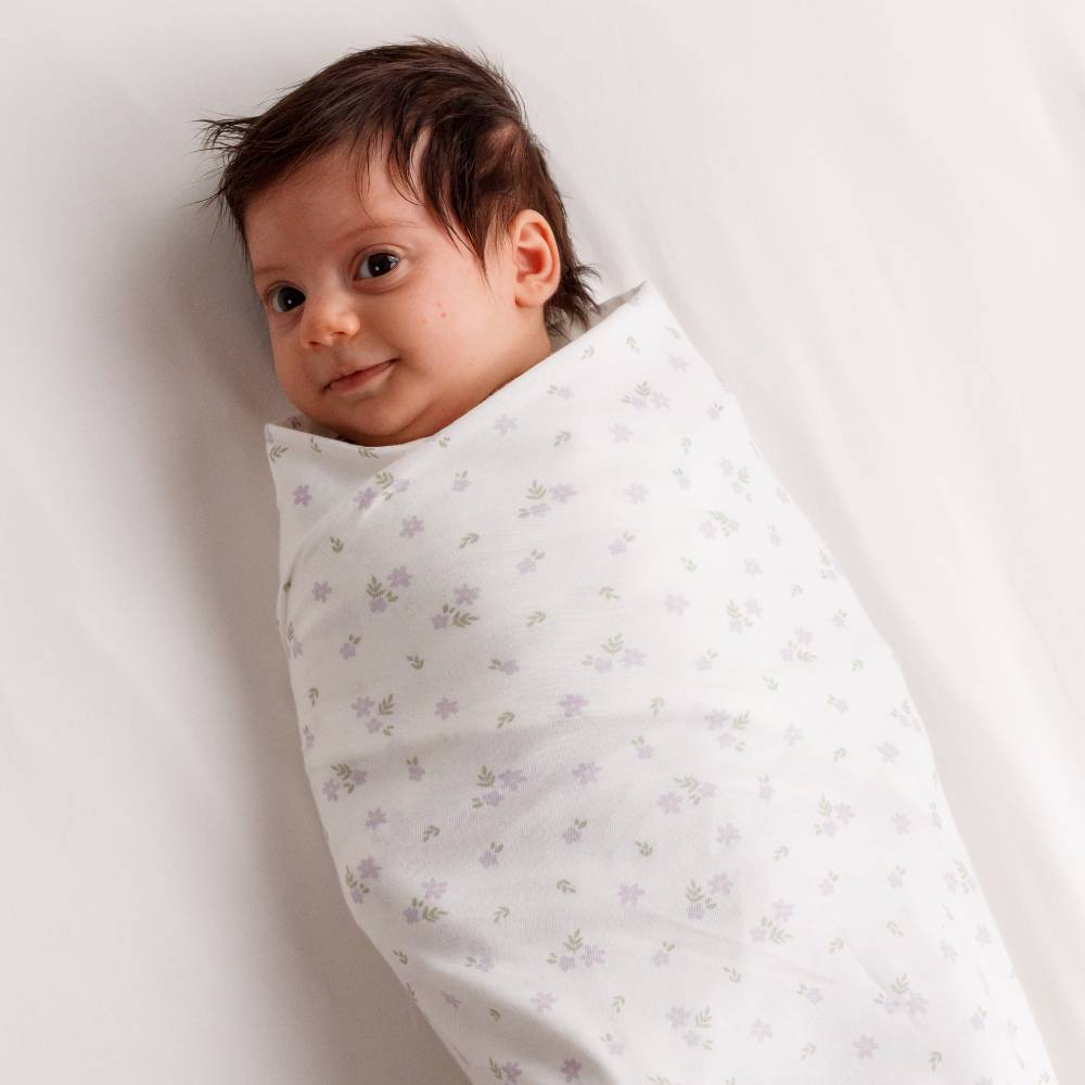 Baby wrapped in a floral-patterned swaddle blanket on a white background