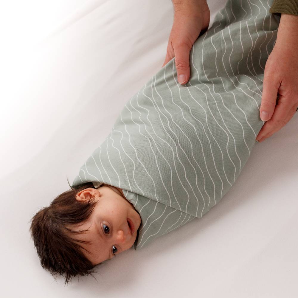 Baby wrapped in a green swaddle with white waves on a white surface