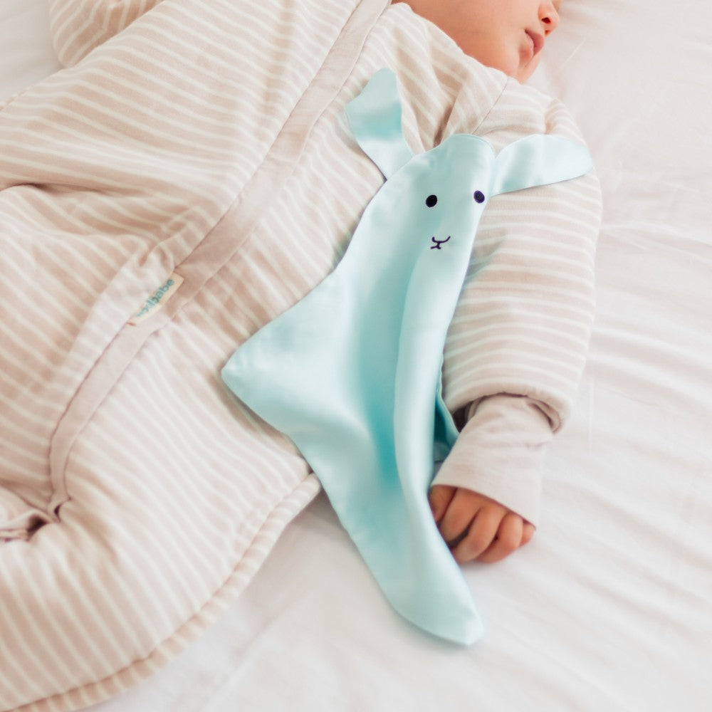Baby holding a light blue silk animal-shaped comfort blanket on a soft surface