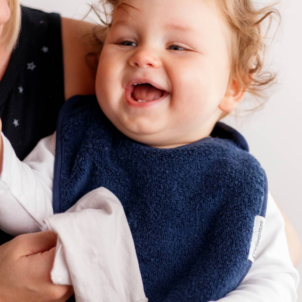Child wearing a navy blue terry cotton towelling bib with a white shirt underneath, held by an adult.