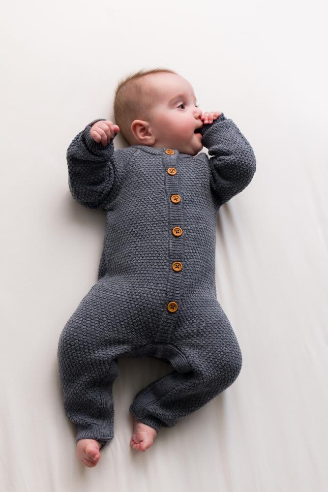Baby wearing a merino wool gray knitted romper with buttons on a white background