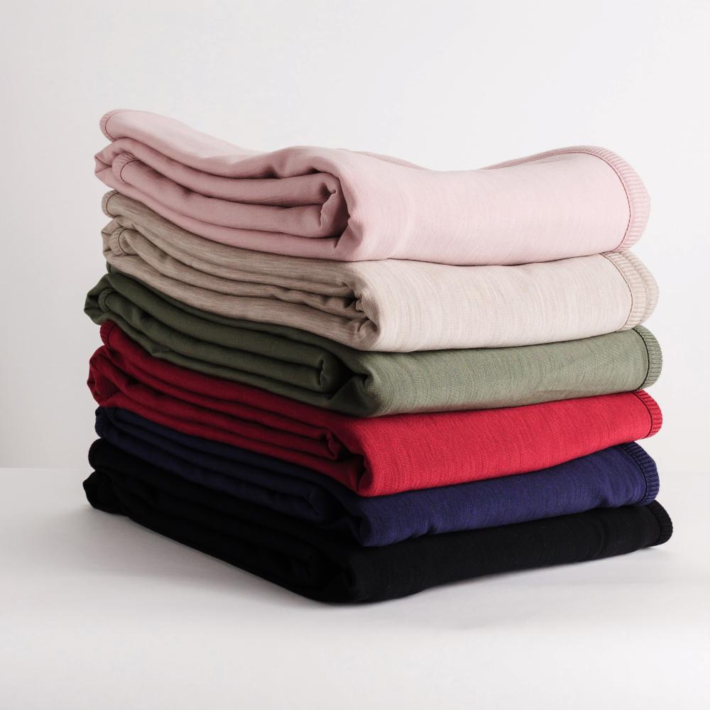 Stack of folded merino fleece/tencel blanket in various colors on a light background