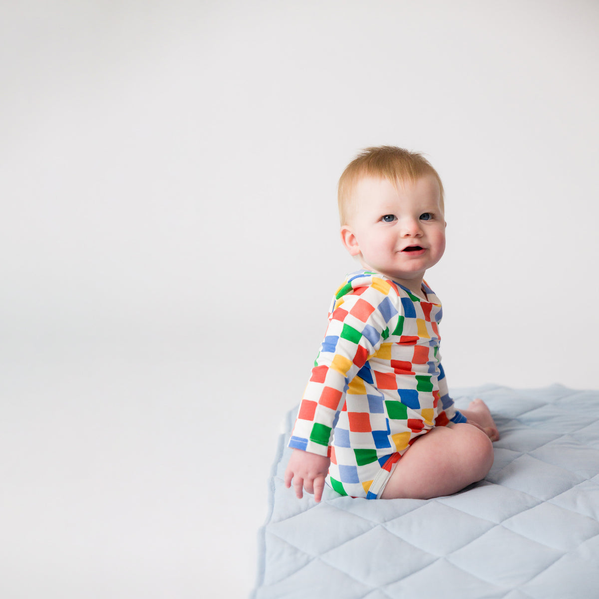 A baby sitting on a playmat wearing a Organic Cotton Long Sleeve Bodysuit - Check.