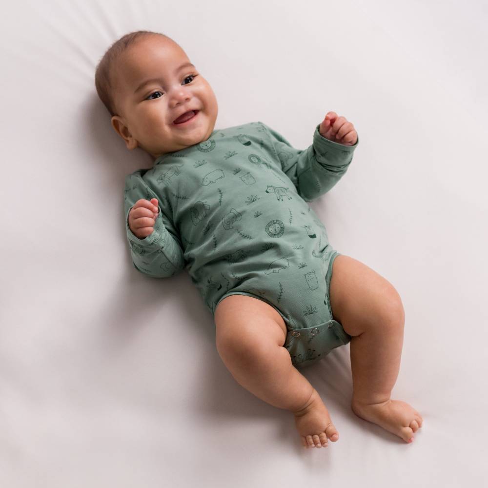 Baby wearing a green organic cotton bodysuit onesie with patterns on a white background