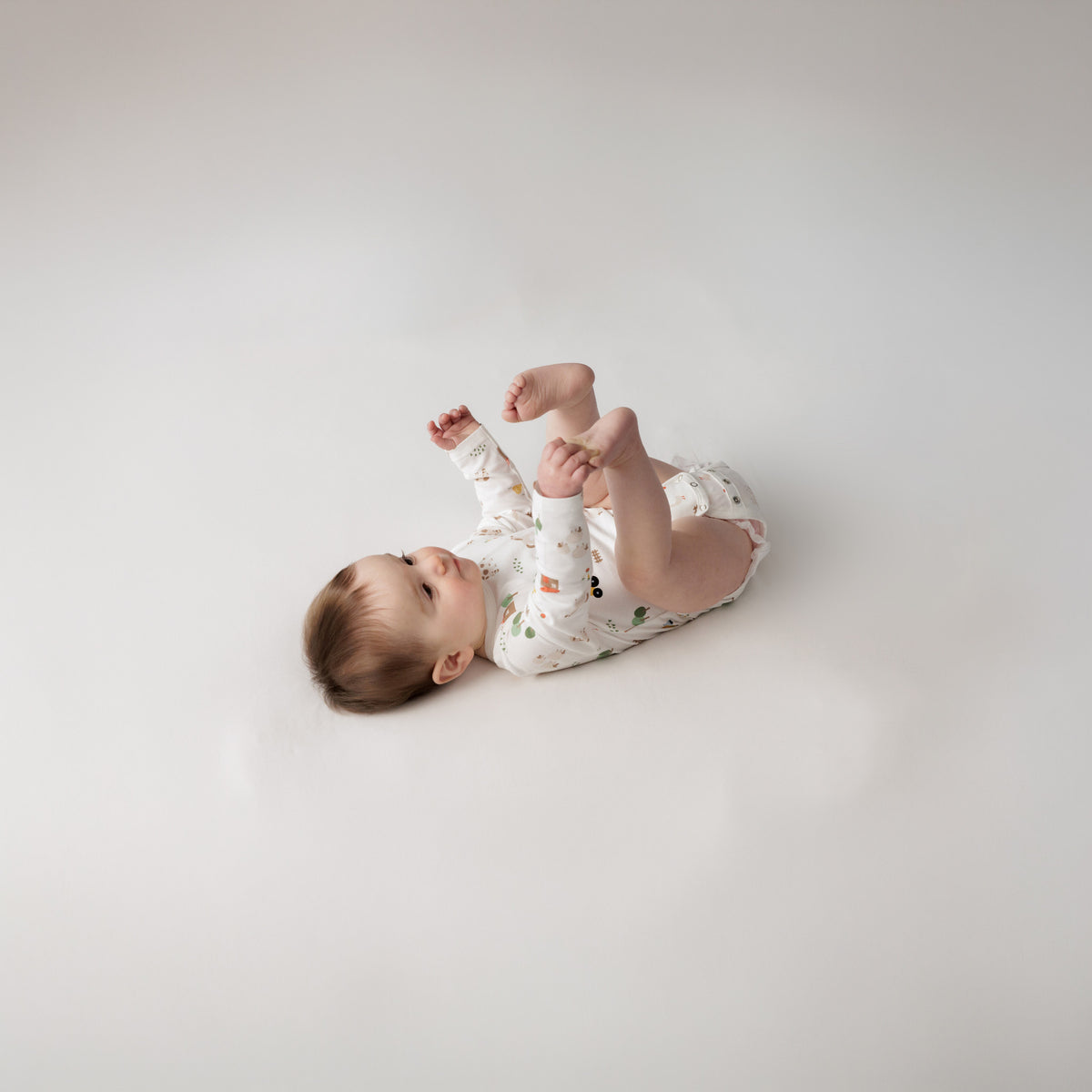 A baby lying down wearing a Organic Cotton Long Sleeve Bodysuit - Farmyard.