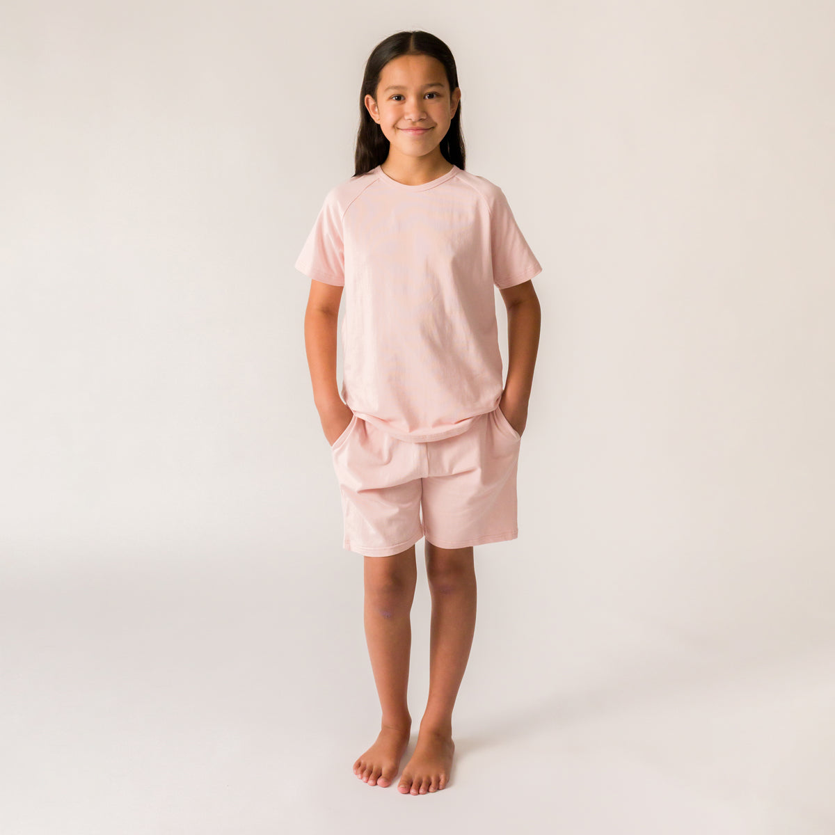 A young girl wearing light pink short sleeve PJs on a light grey background. 