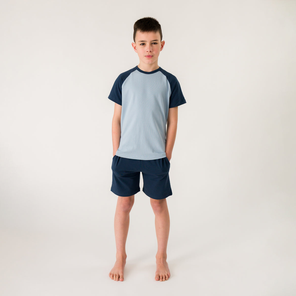 A boy standing wearing blue summer pyjamas. 