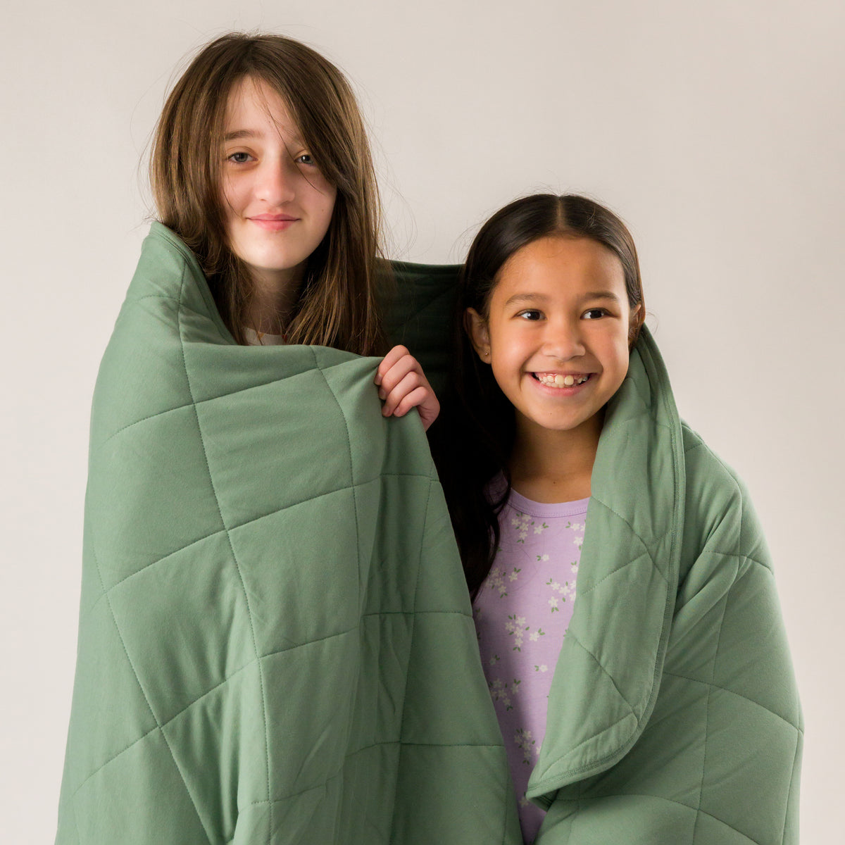 Two young children wrapped in a fern green quilted blanket. 