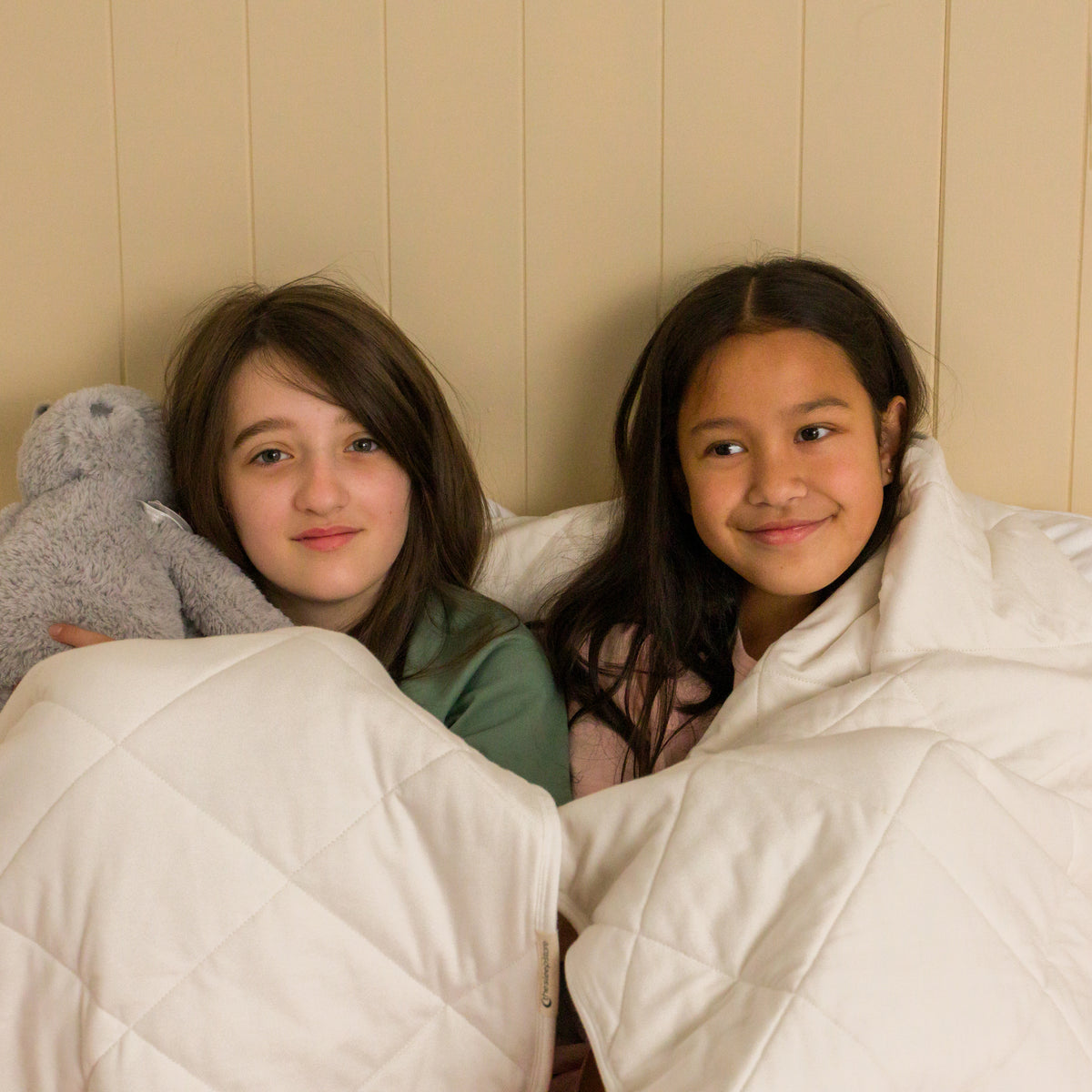 Two young children snuggled in a natural cream quilted blanket. 