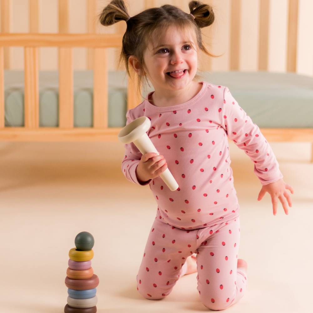 Child in pink strawberry pajamas holding a toy in a crib