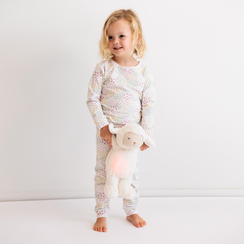 Child wearing a white pajama set with a pattern, holding a plush toy with a light-up feature, on a plain background.